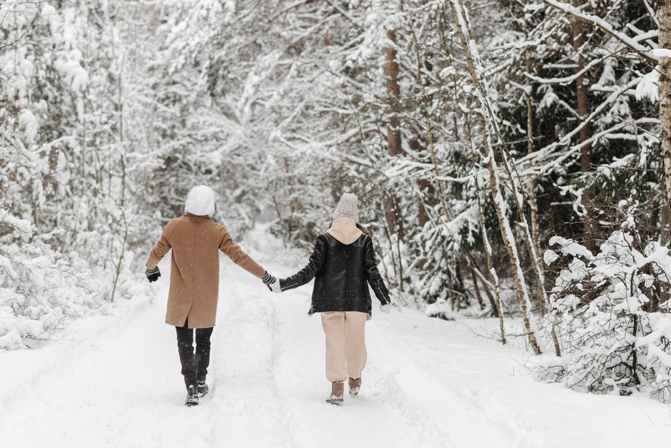 A couple holding hands walking in a snow-covered forest during winter.