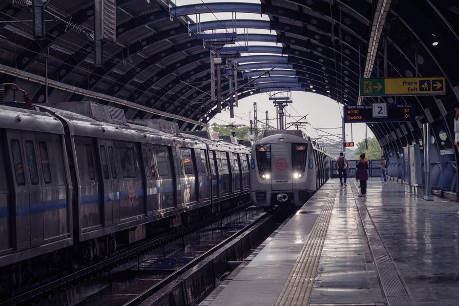 A metro train arrives at a New Delhi station on a rainy day, capturing the city's urban tr