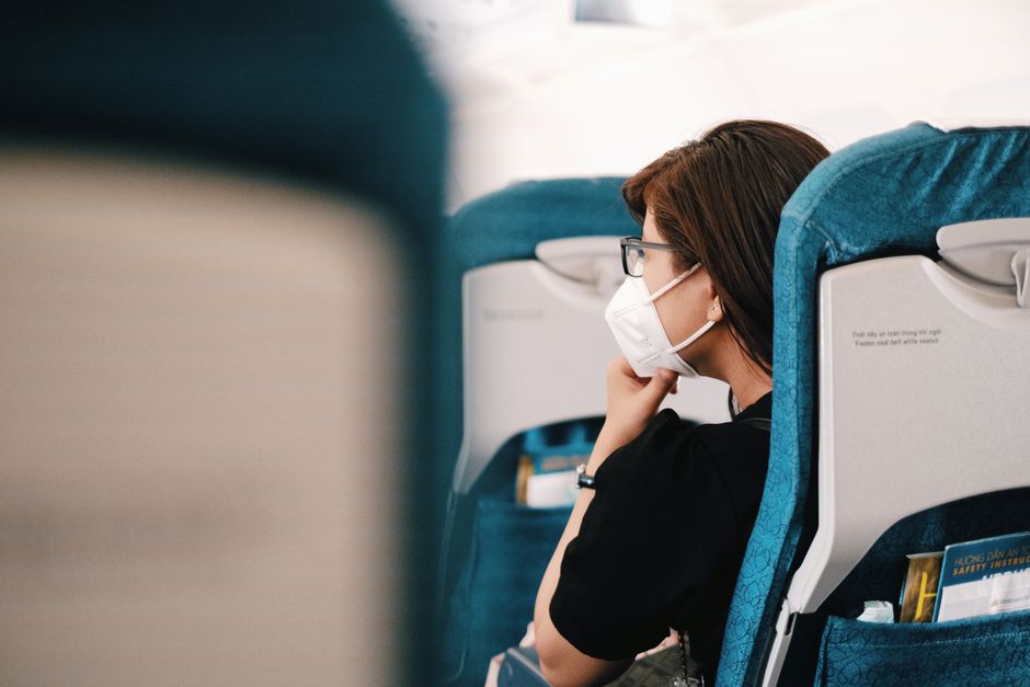 A woman sits on an airplane, wearing a face mask during the flight, representing the new n