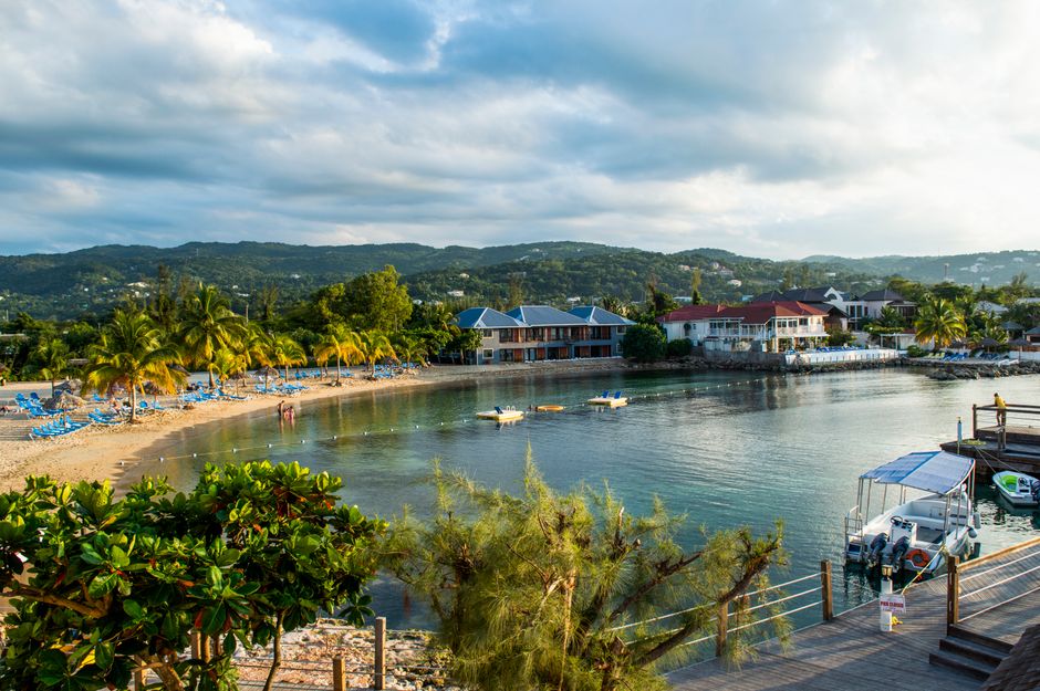 Settlement with cottages near forested mountains situated on sandy beach and pier with trees