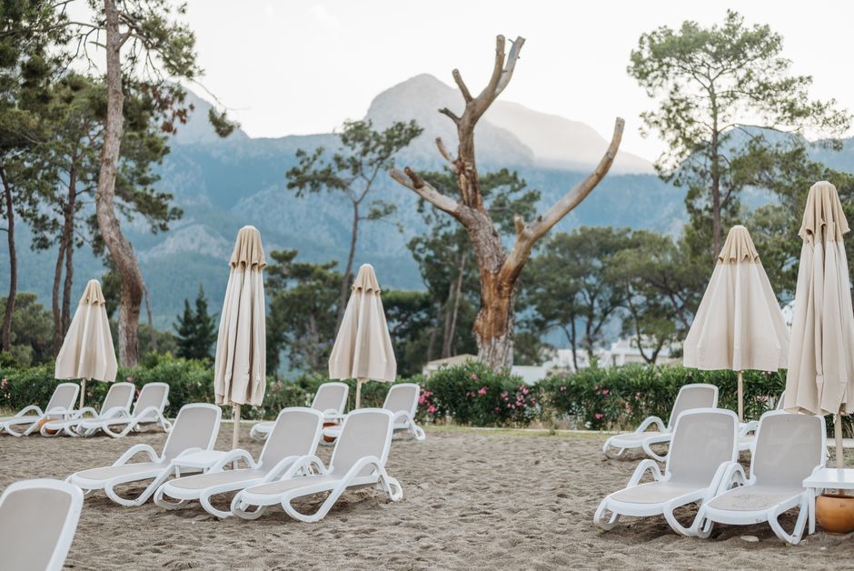 Tranquil beach scene with sunloungers and umbrellas at a resort near mountains, surrounded by greenery.