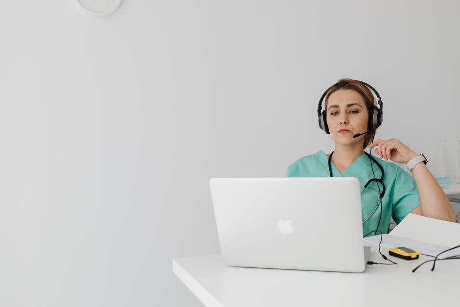 Woman doctor in scrub suit conducting online consultation on a laptop from an office.