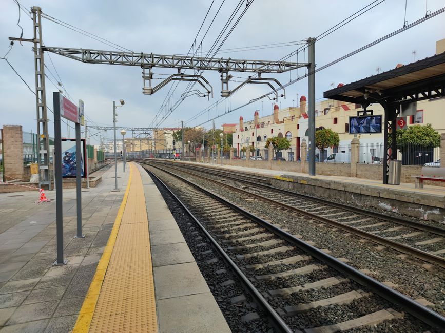 Wide view of railway tracks and platform at Dos Hermanas station on a cloudy day in Andalucía, Spain.