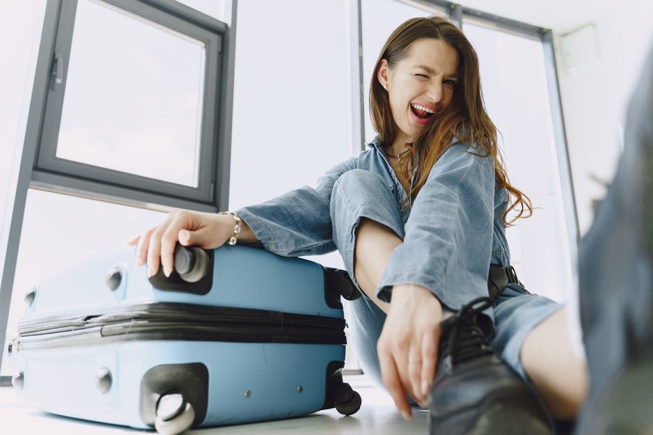 Low angle of young exited female traveler with suitcase in stylish outfit having fun before flight