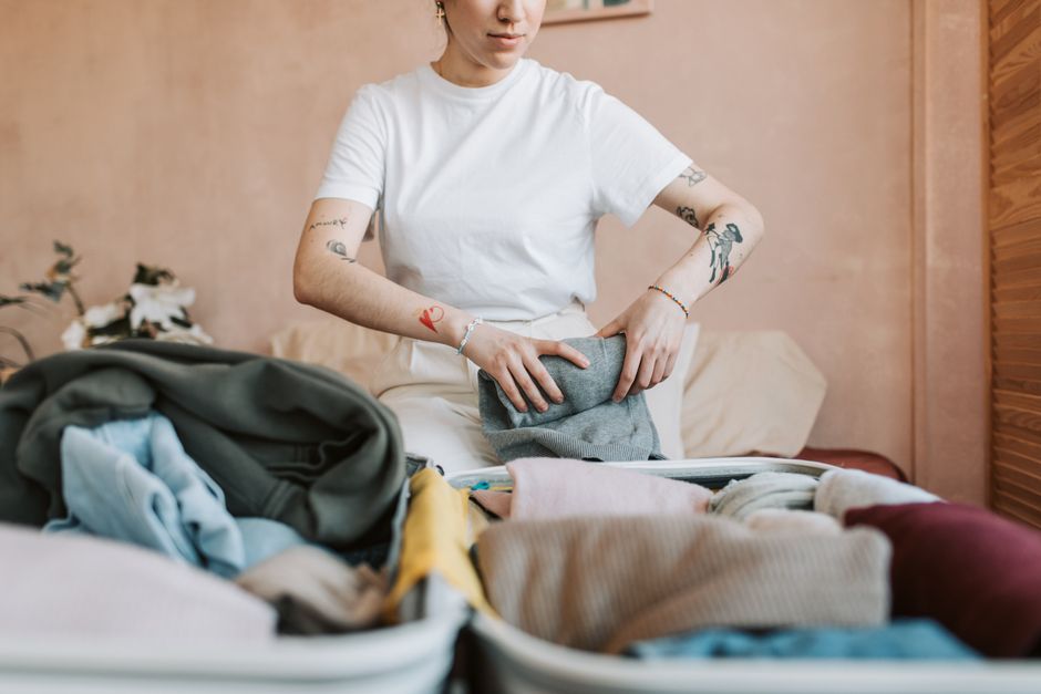 A woman with tattoos packs a suitcase full of clothes, preparing for travel.