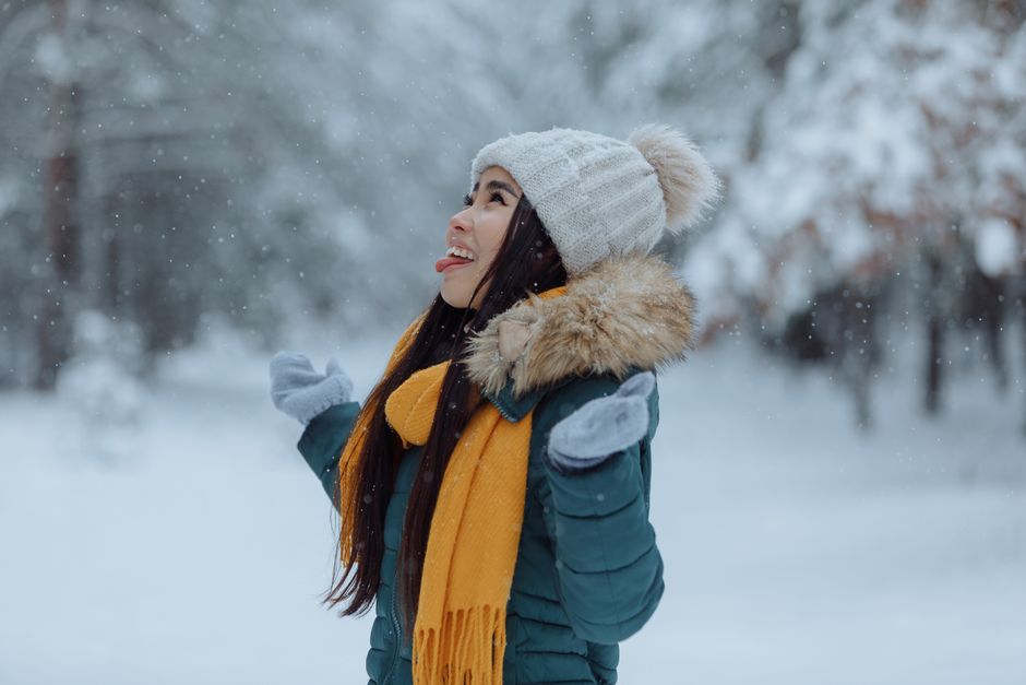 Happy woman in winter attire enjoying the snowfall with a playful expression outdoors.