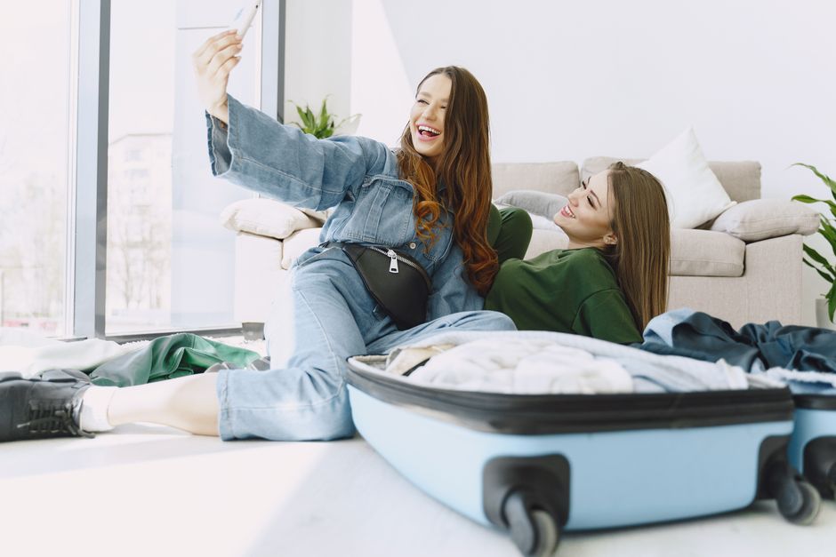 Happy young female friends in trendy outfits having fun and taking selfie while packing su