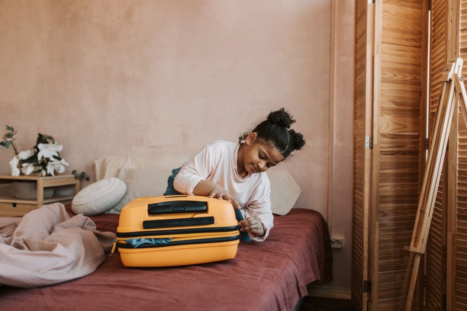 A young girl packs a bright yellow suitcase on a bed, preparing for travel.