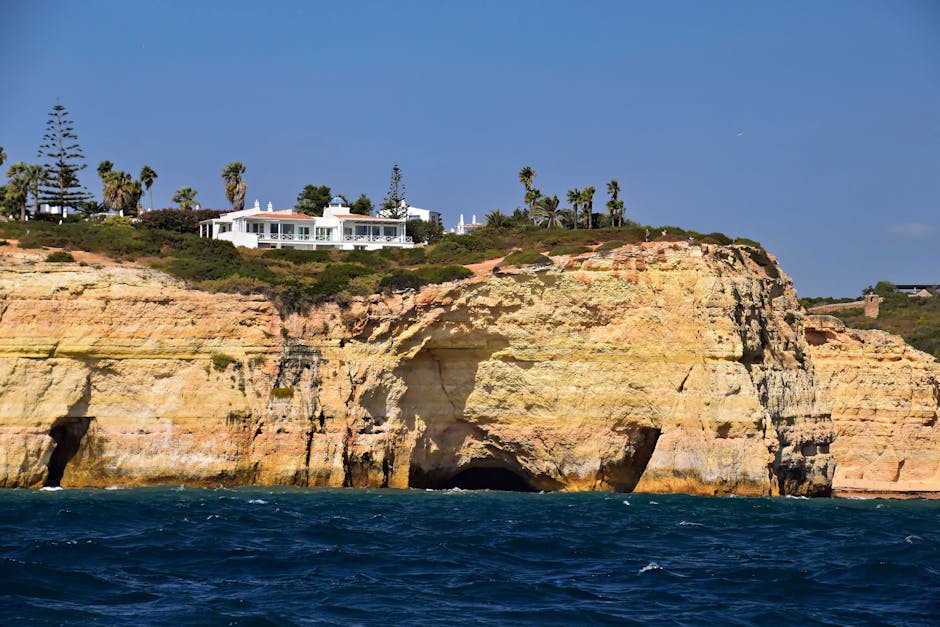 A stunning view of Algarve's sea cliffs with a villa on top, under a clear blue sky.