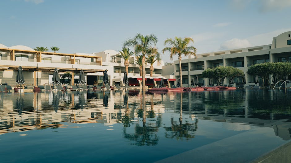 Elegant resort with a pool and palm trees under a clear blue sky in Greece.