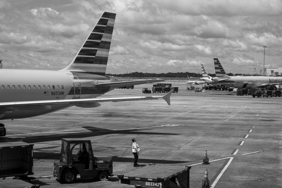 Black and white image of airplanes on a busy airport tarmac with a worker in view.