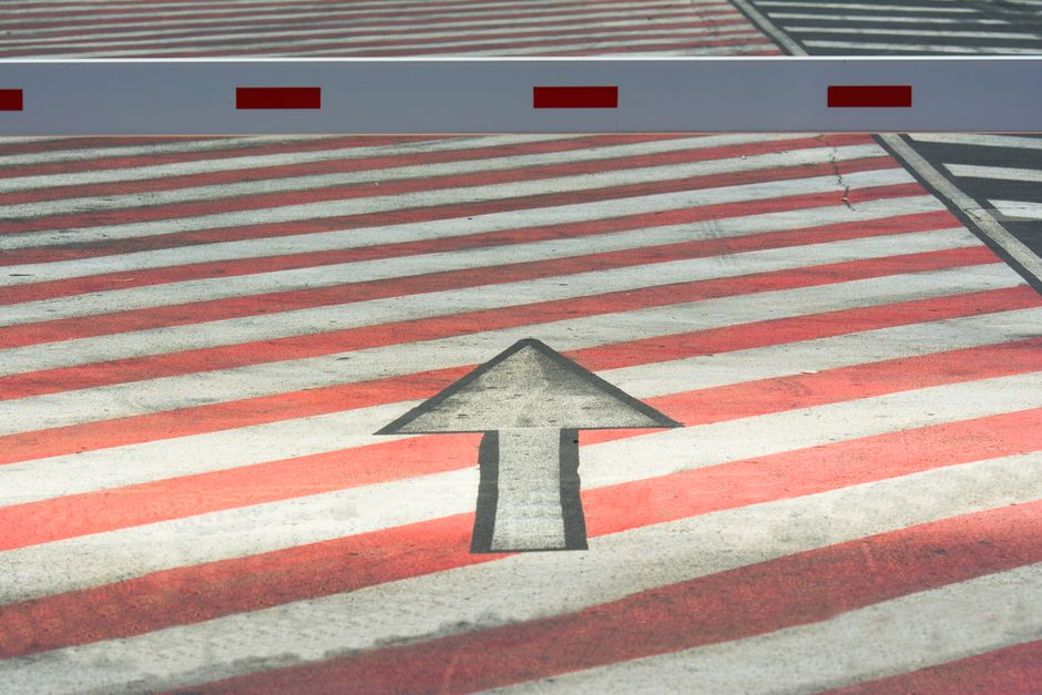 A zebra crossing with a prominent directional arrow, featuring red stripes and a barrier.