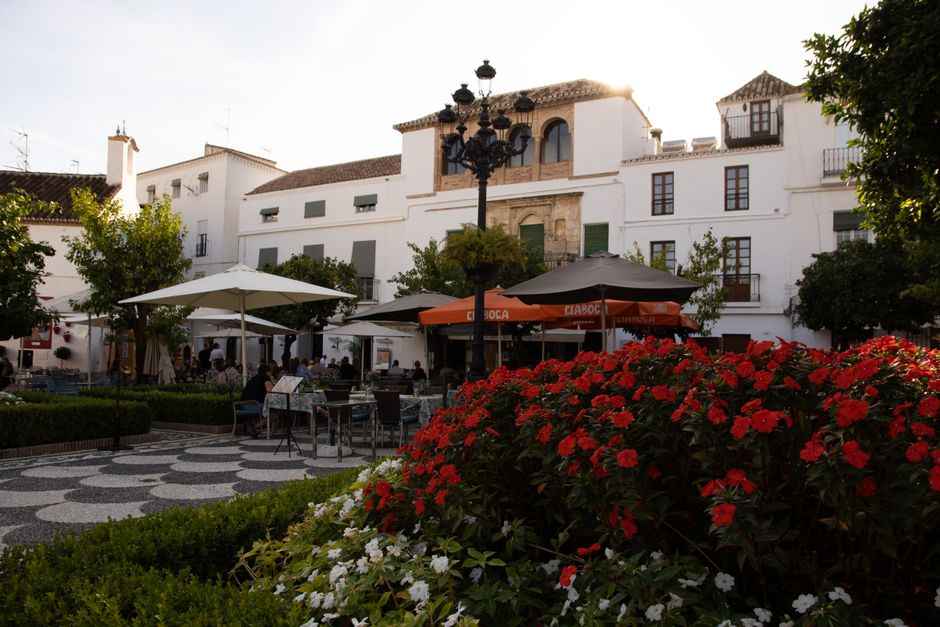 Picturesque outdoor cafe with vibrant flowers and umbrellas in a European courtyard.