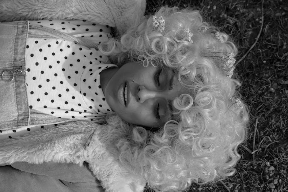 A woman with a curly wig and polka dot outfit resting outdoors in grayscale.