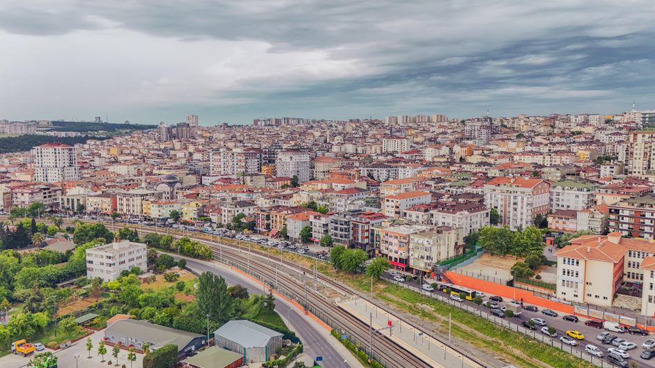 Aerial view of dense urban architecture with roads and greenery under cloudy skies.
