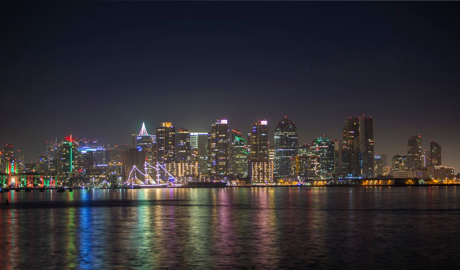 Vibrant nighttime cityscape with illuminated skyscrapers reflecting on the calm sea.
