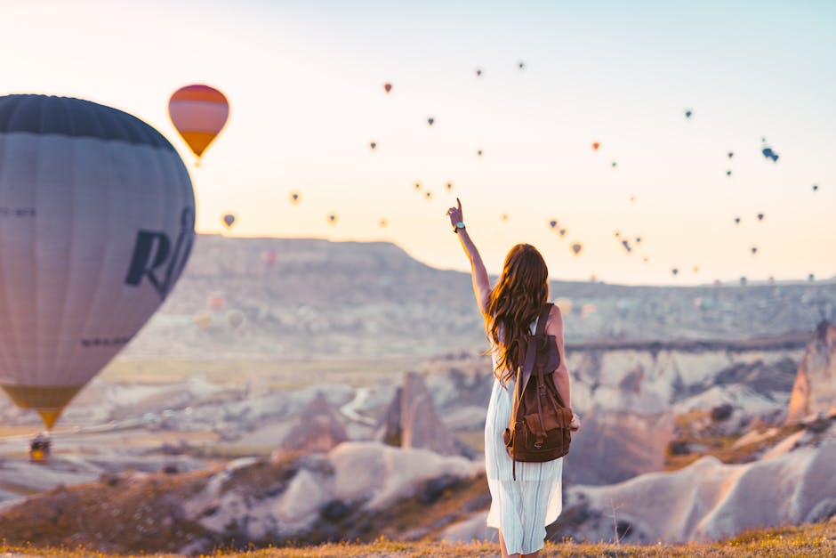 A woman points at colorful hot air balloons over Cappadocia at sunrise.