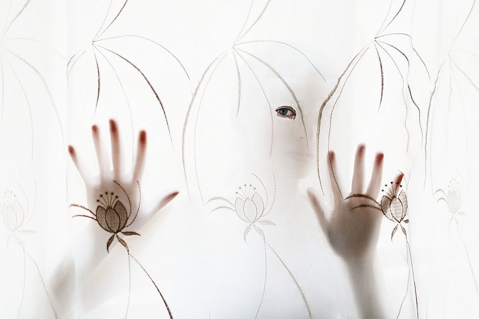 Artistic silhouette of a person with hands and eye visible through a decorative curtain.