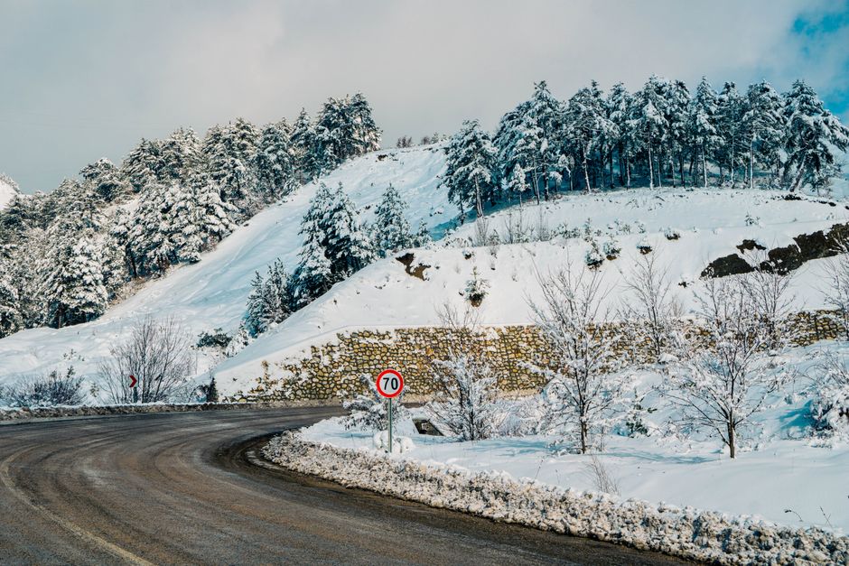 A scenic snowy road curves through a wintery forest landscape with snow-covered trees.
