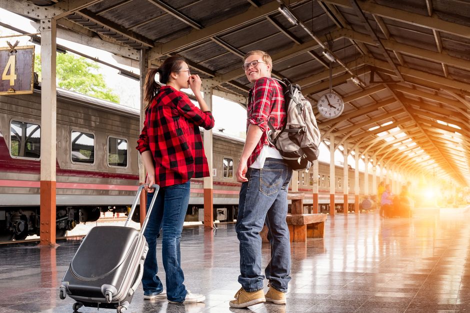 Young couple in a railway station, ready for travel. Bright morning scene with backpacks a
